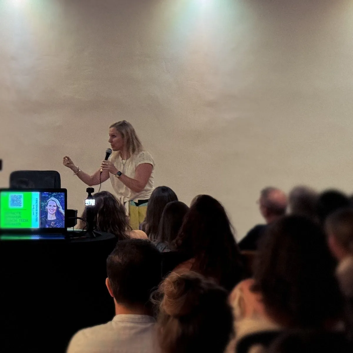 Kirsten speaking to a full room, filmed and photographed by the audience