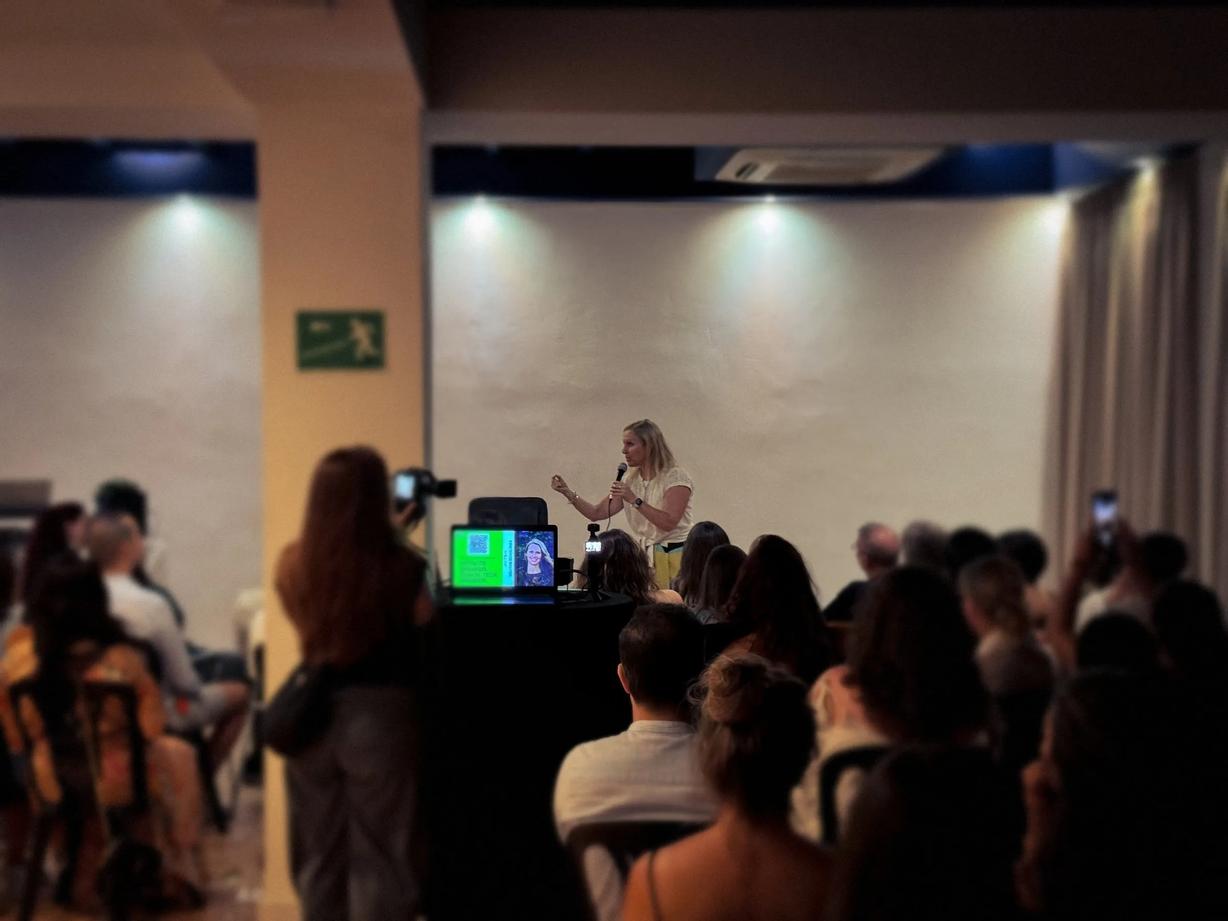 Kirsten speaking to a full room, filmed and photographed by the audience