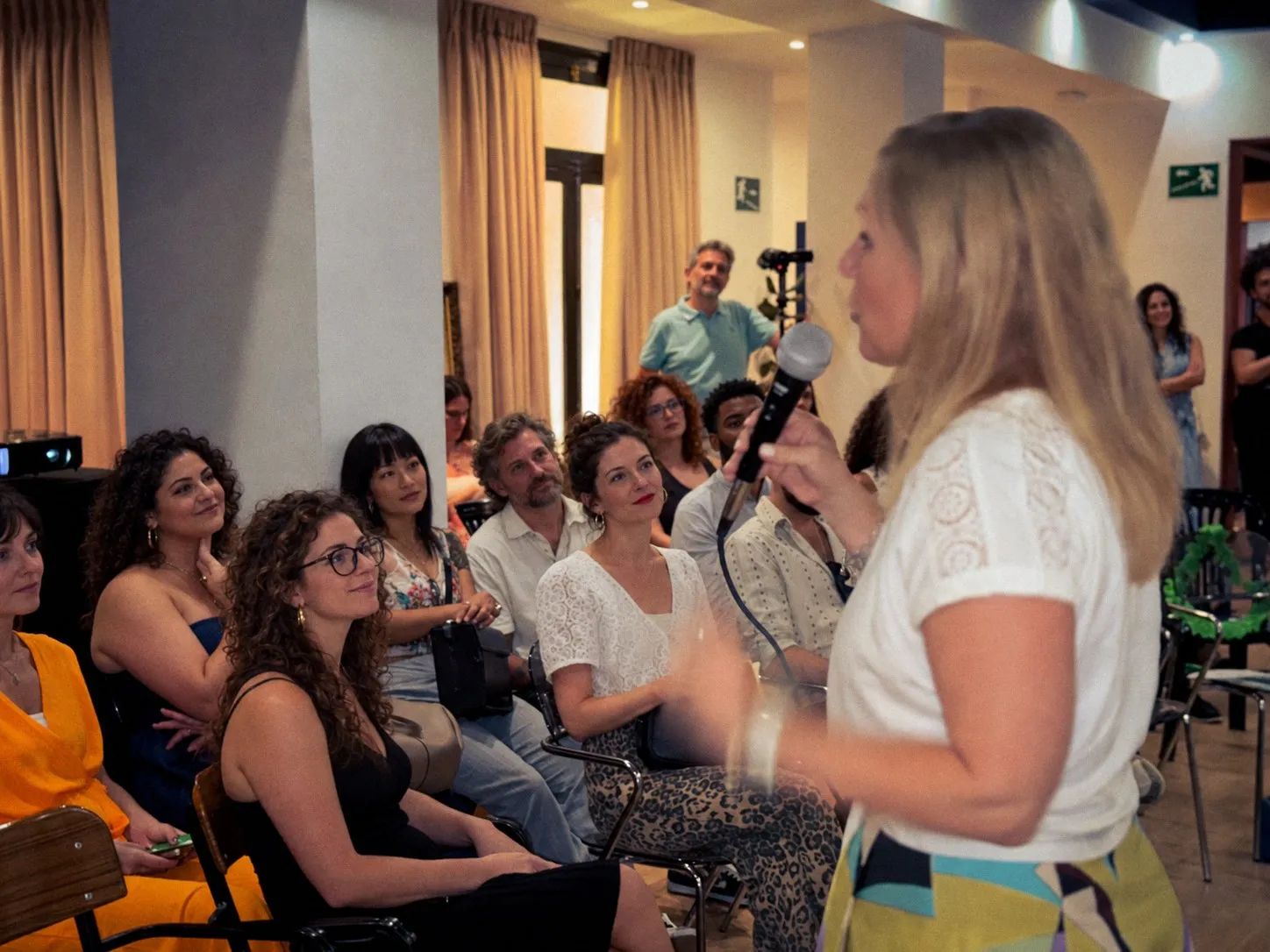 Kirsten speaking into a microphone, the audience smiling as they listen
