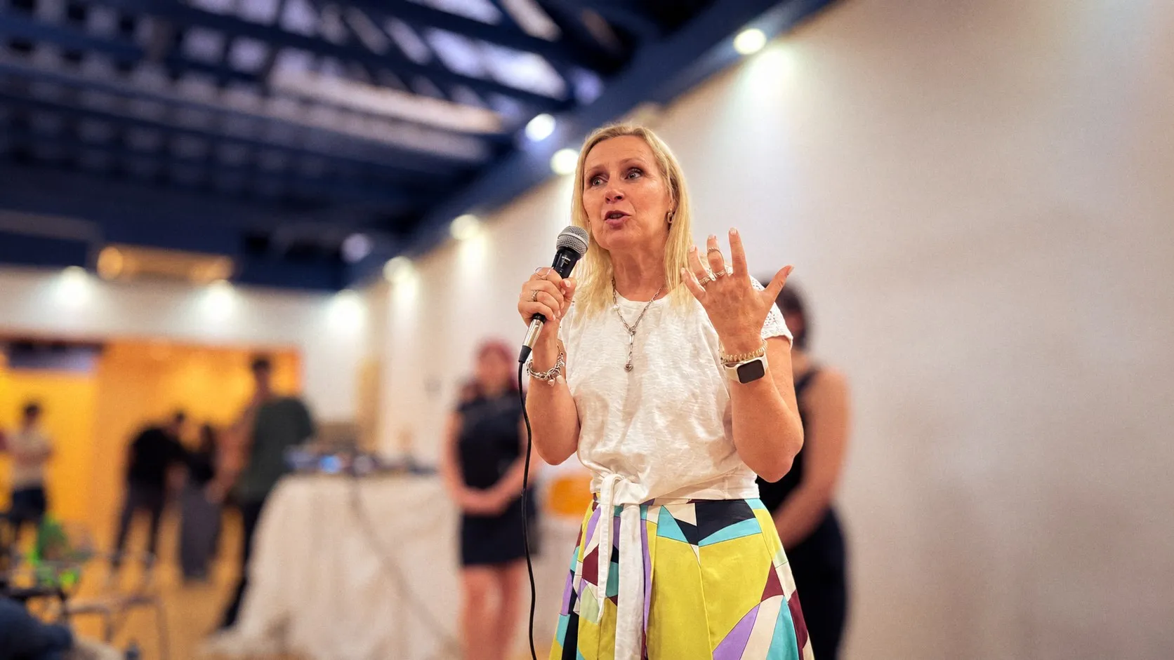 Kirsten speaking into a microphone, gesturing as she makes a point