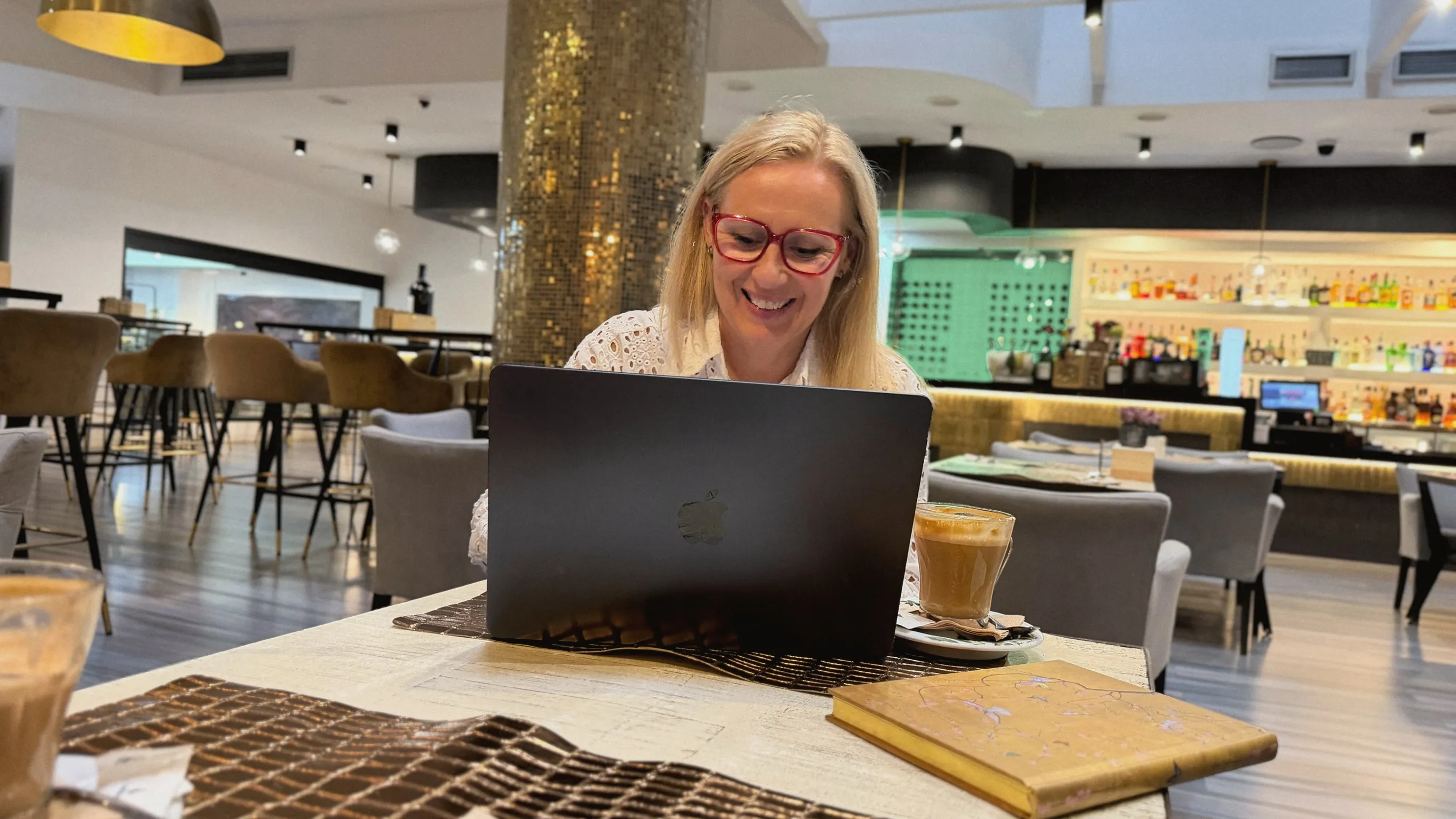 Kirsten smiling at her laptop in a café