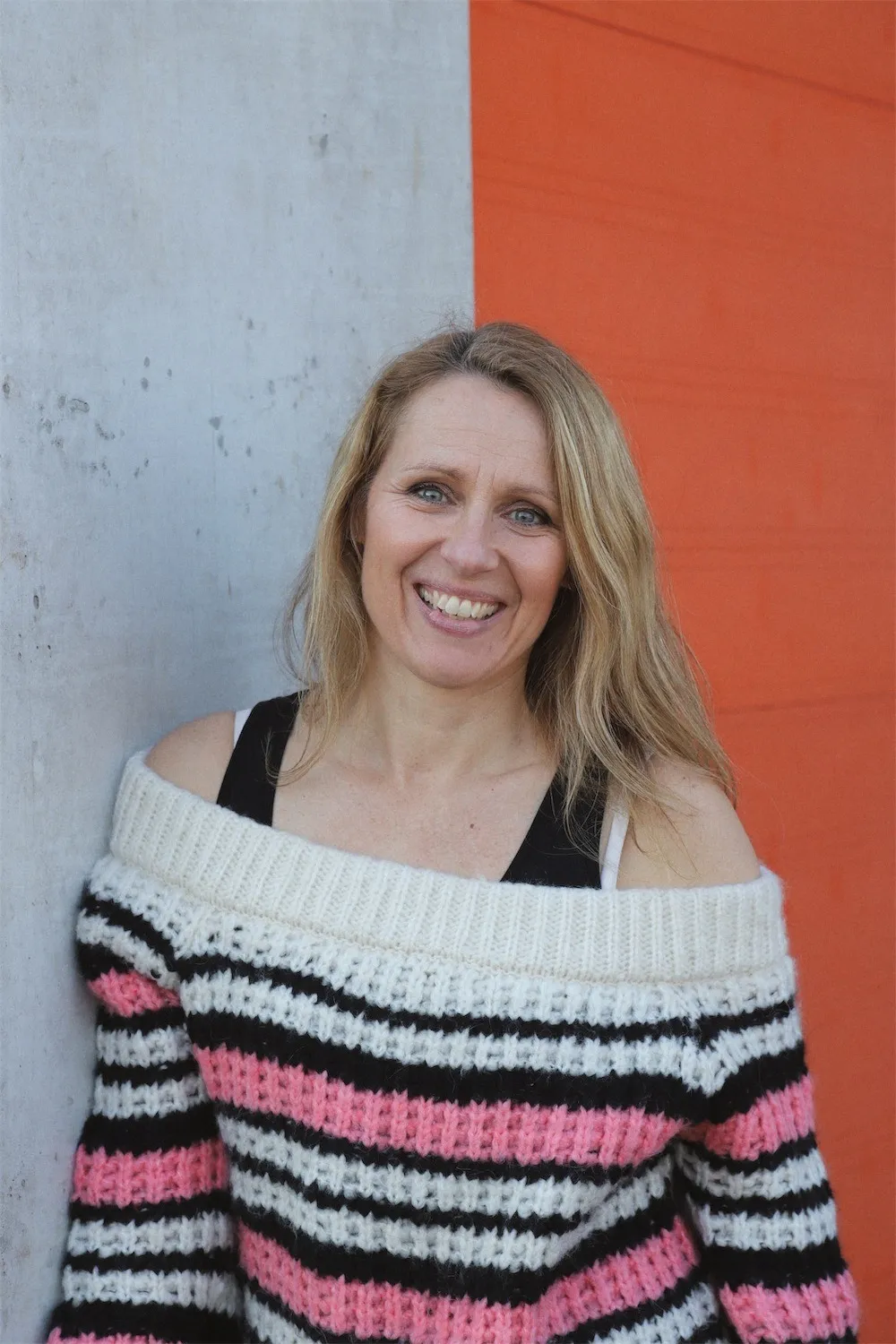 Kirsten smiling, leaning against a grey and orange wall